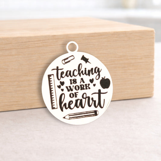 Circular pendant with 'Teaching is a Work of Heart' text on a wooden block.