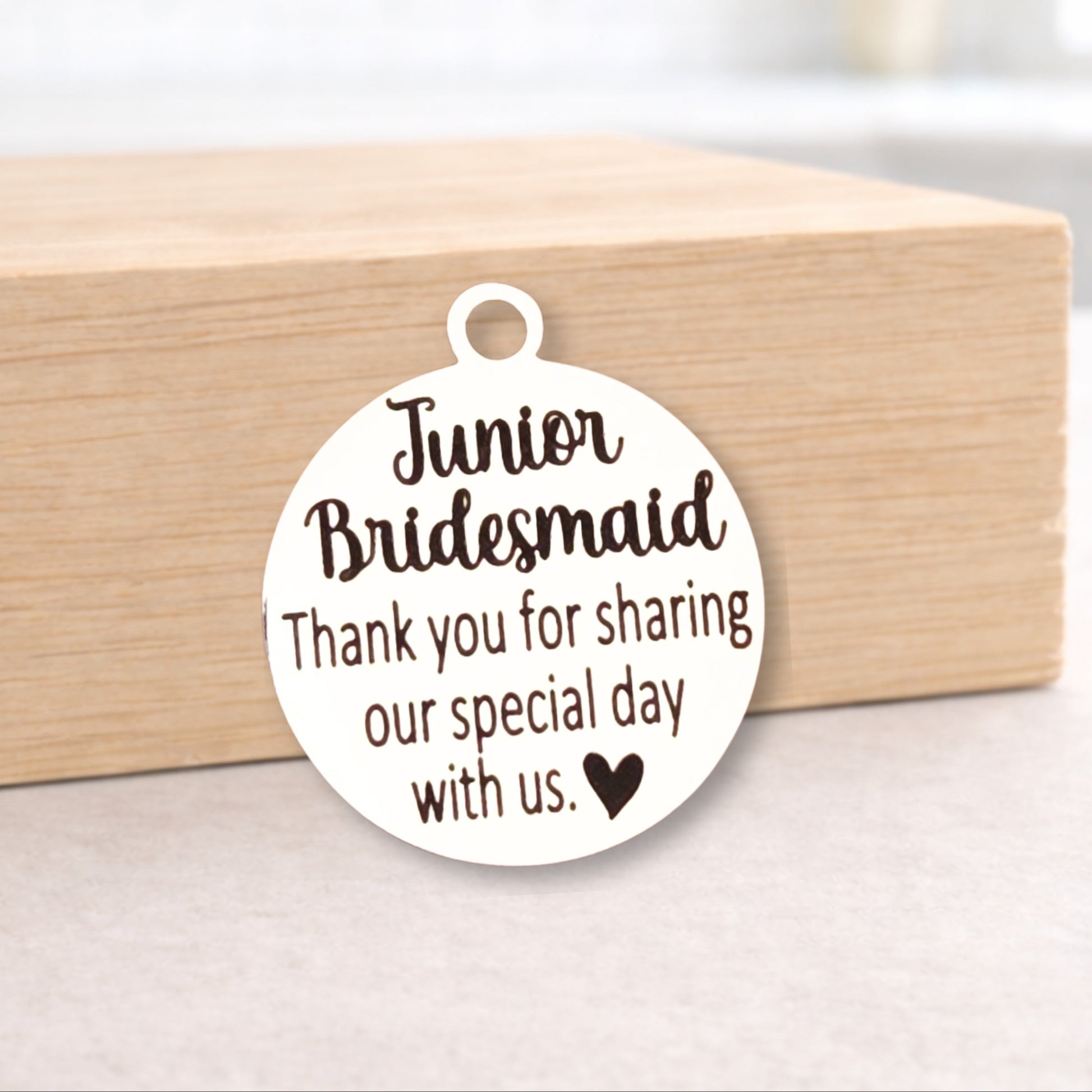Round metal tag with 'Junior Bridesmaid' text on a wooden block