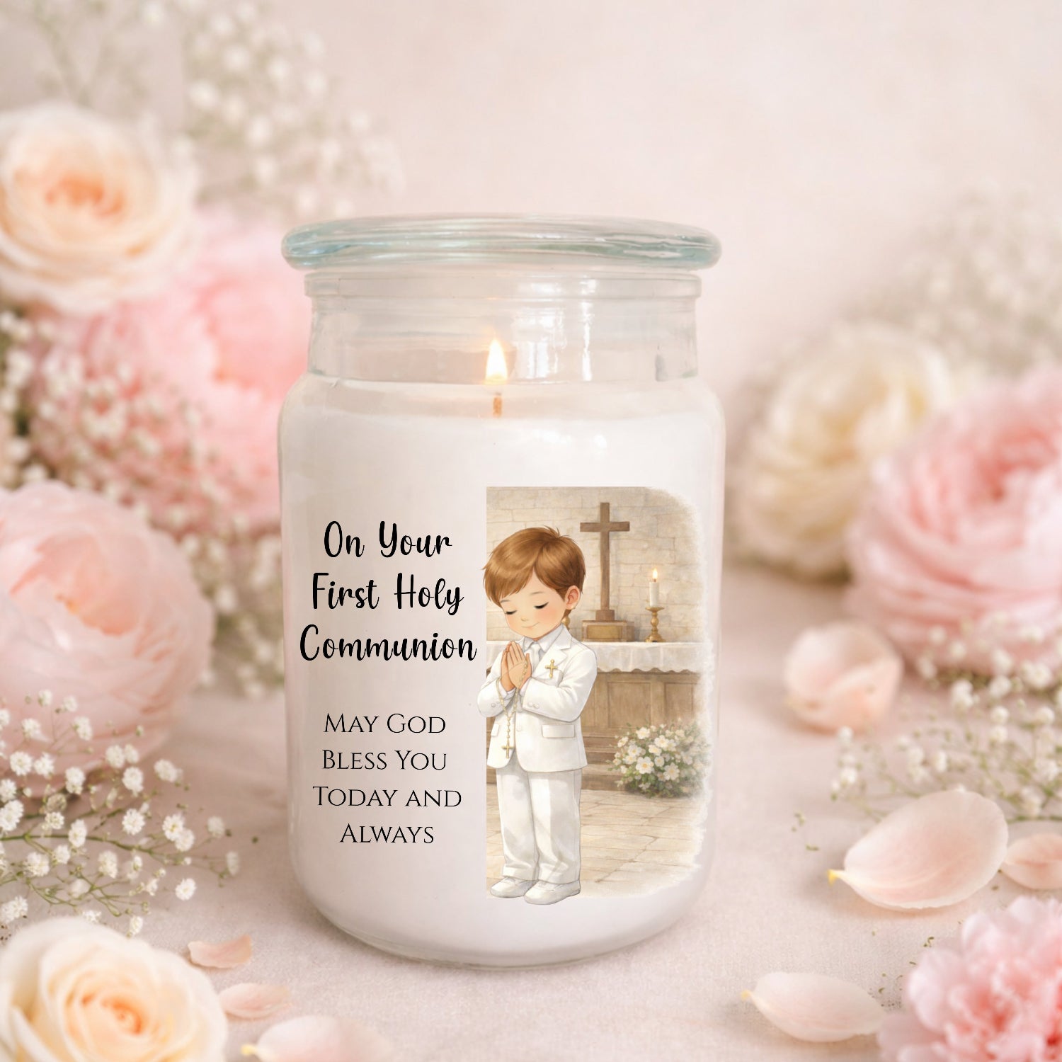 Candle in a glass jar with a printed design of a child in a white robe and text, surrounded by pink flowers.