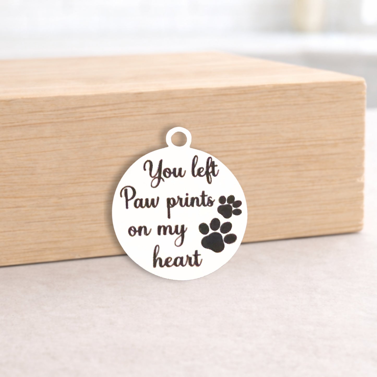 Round metal pendant with engraved text and paw prints on a wooden block.