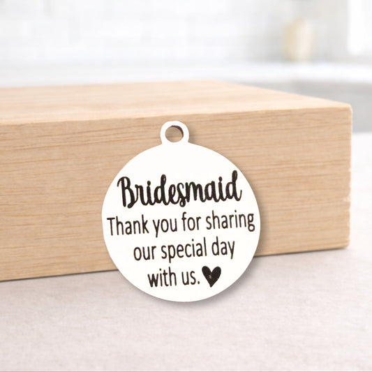 Round white pendant with 'Bridesmaid Thank you for sharing our special day with us' text on a wooden block.