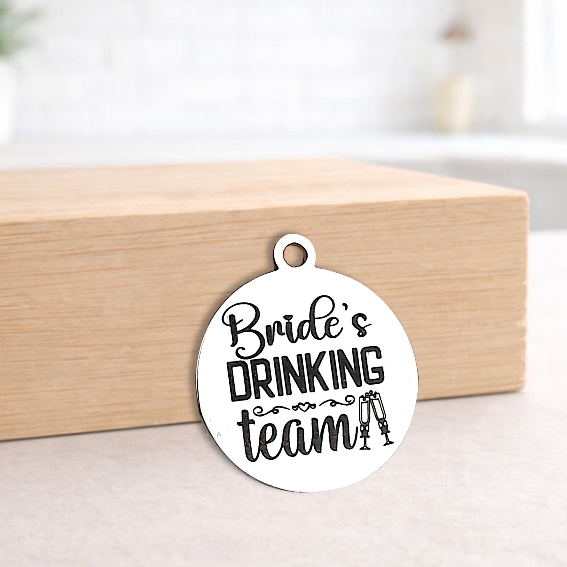 Circular metal pendant with 'Bride's Drinking Team' text on a wooden block.
