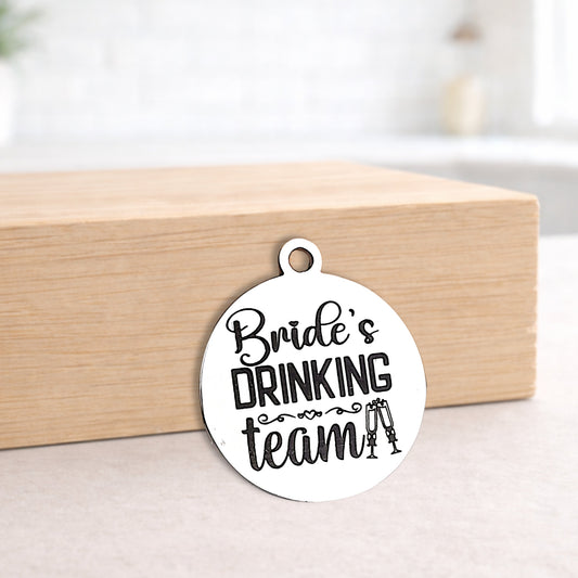 Circular metal pendant with 'Bride's Drinking Team' text on a wooden block.