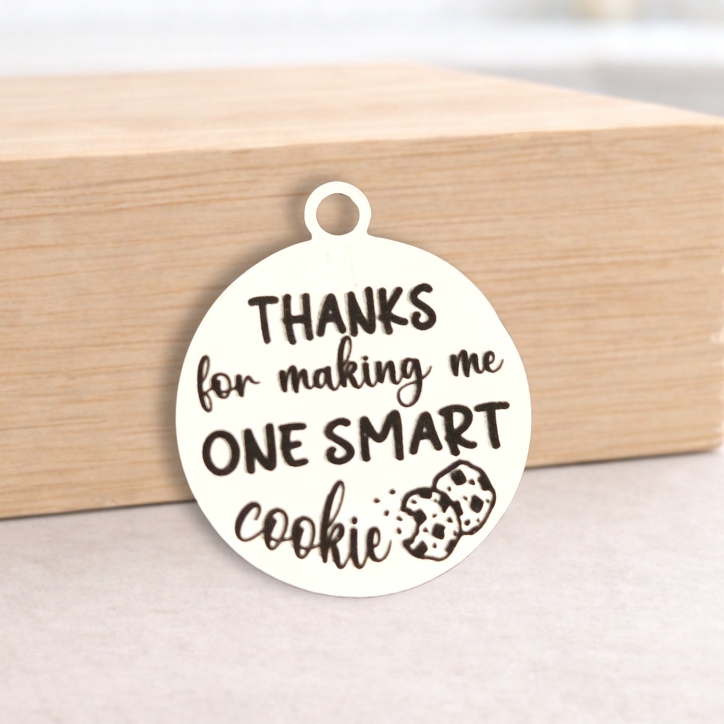 Round white pendant with text 'Thanks for making me one smart cookie' on a wooden block.