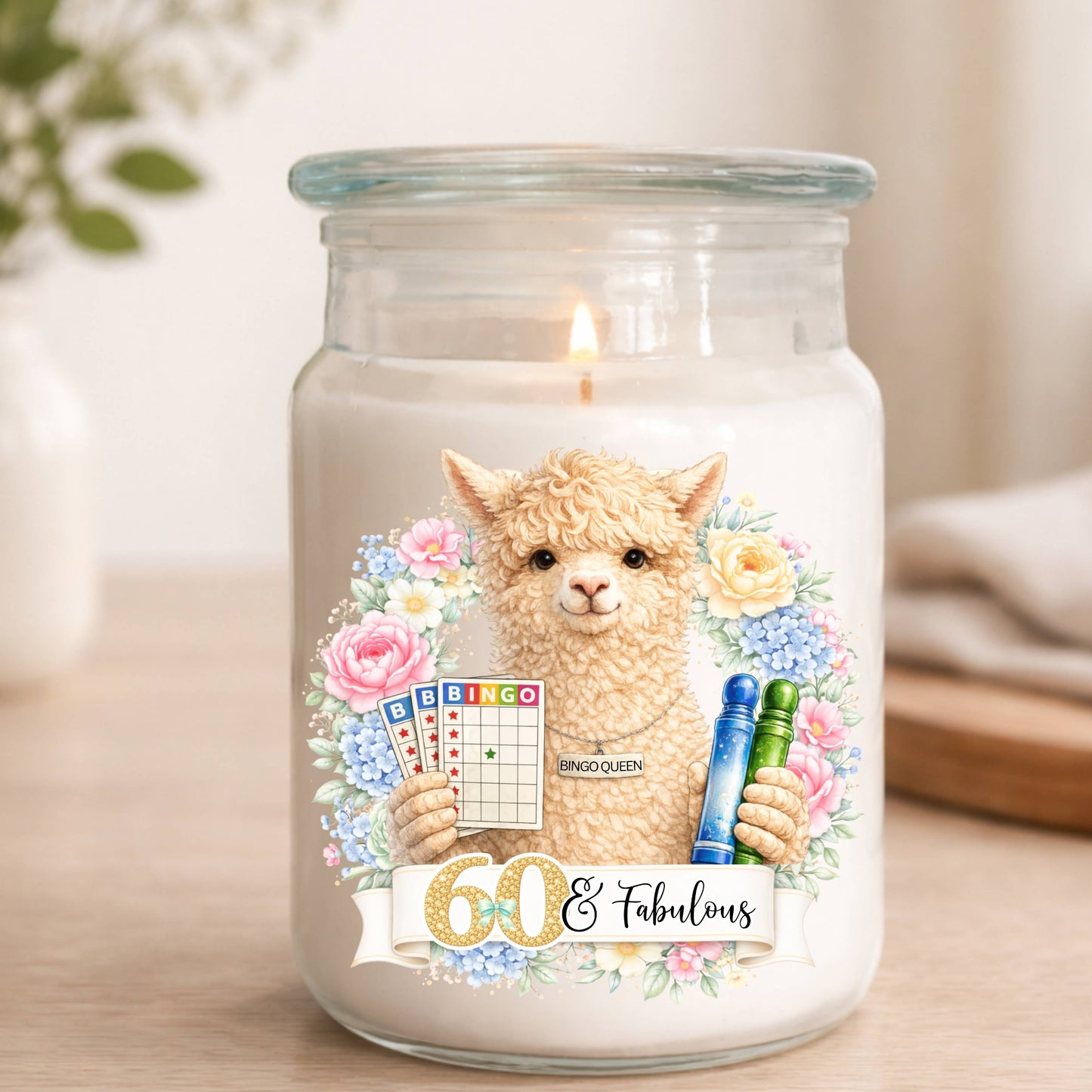 Candle in a jar with a decorative label featuring an alpaca and birthday text, on a wooden surface.