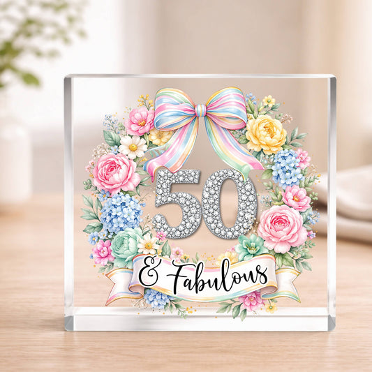 Decorative glass block with floral design and '50 & Fabulous' text on a wooden surface.