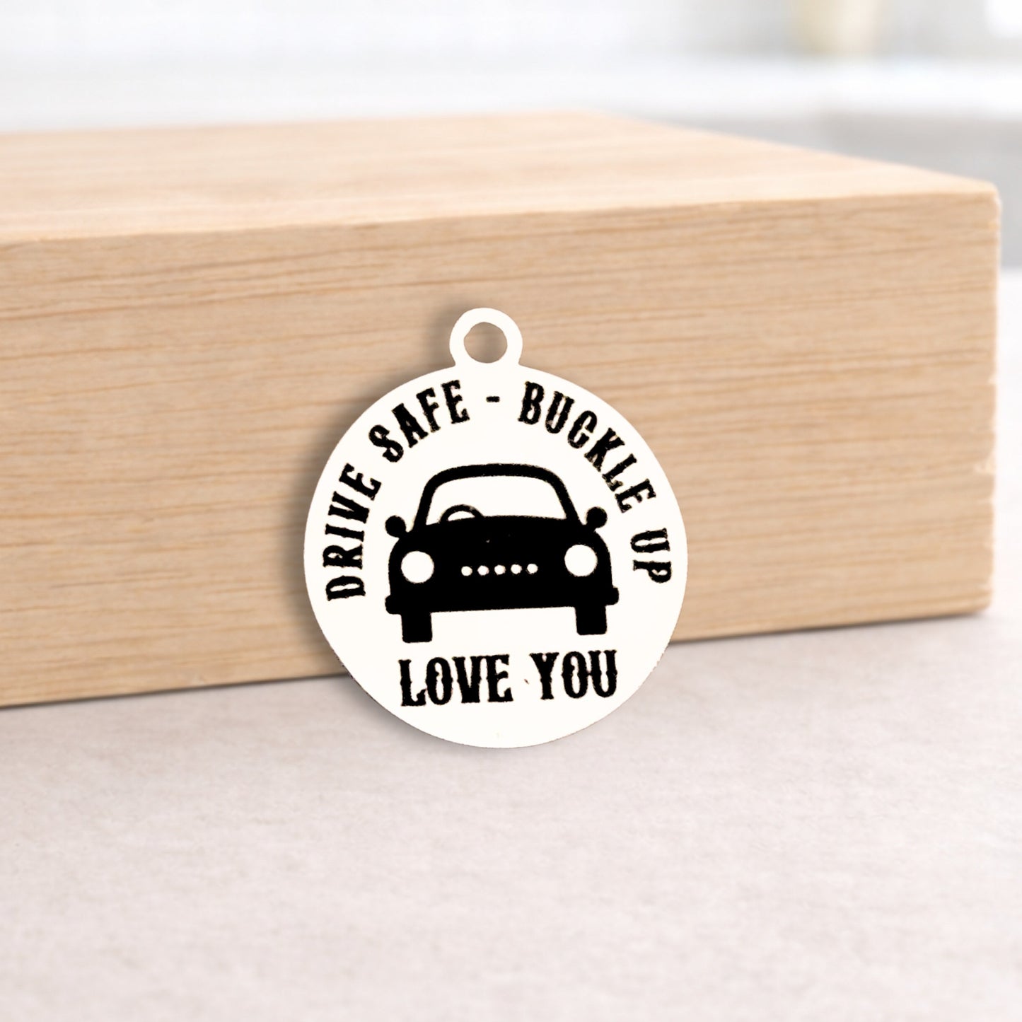 Round metal charm with text 'Drive Safe, Buckle Up, Love You' on a wooden block.