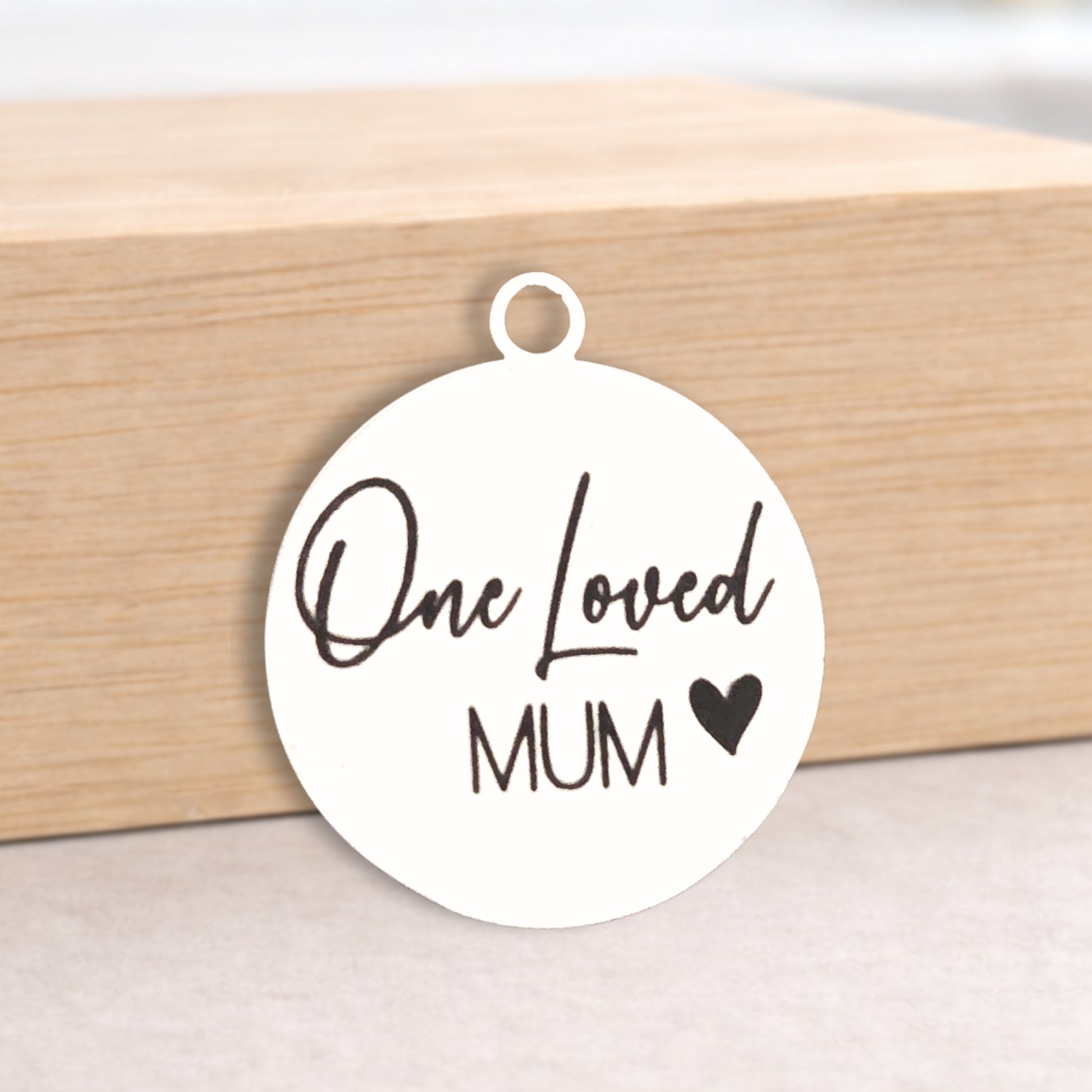 Round white pendant with 'One Loved Mum' text on a wooden block