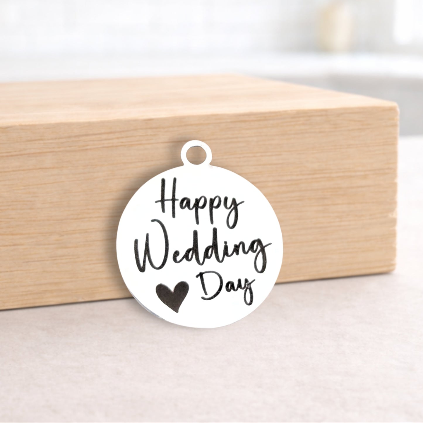 Round metal pendant with 'Happy Wedding Day' text on a wooden block