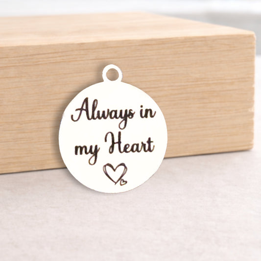 Round white pendant with 'Always in my Heart' text on a wooden block.