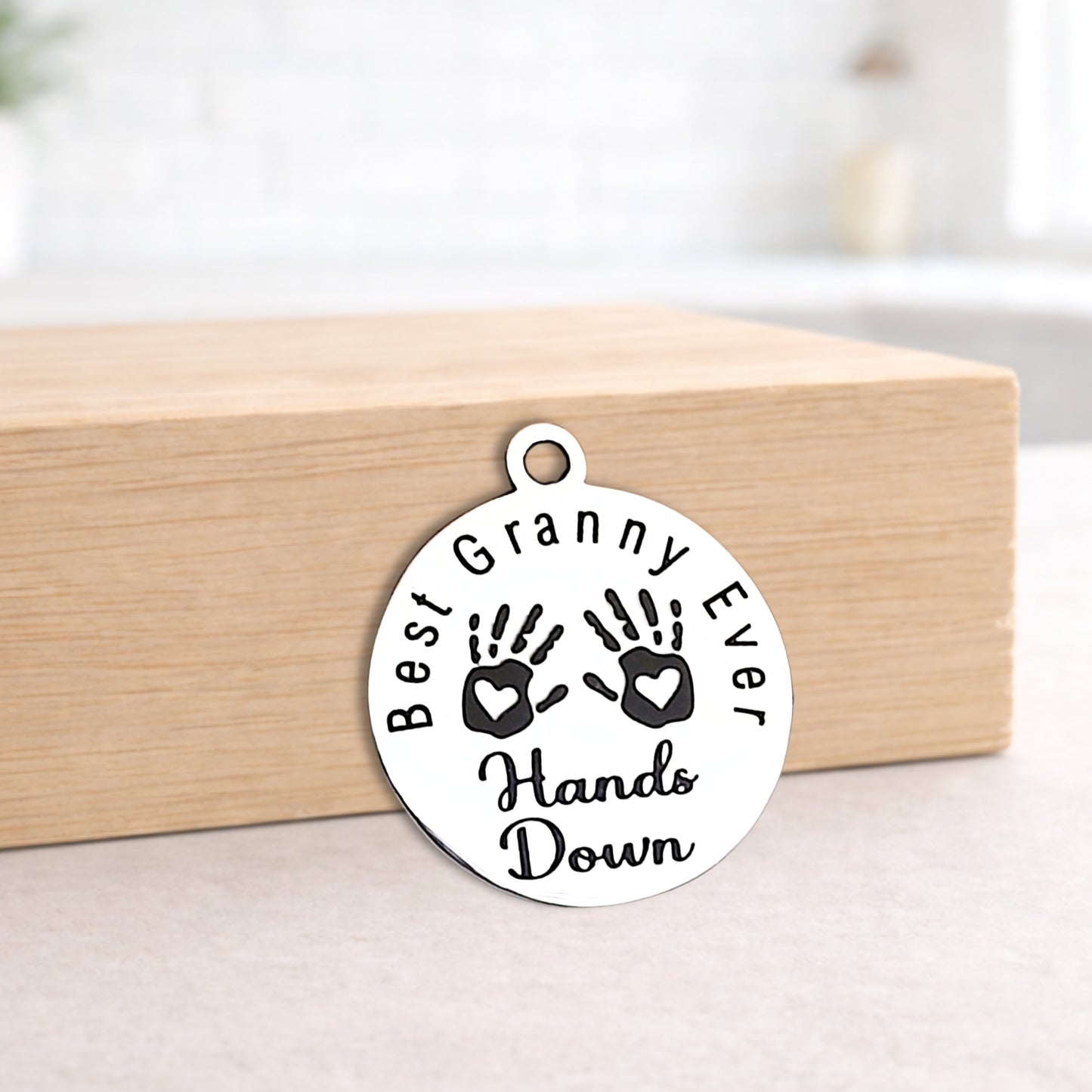 Round silver pendant with 'Best Granny Ever Hands Down' text on a wooden block.
