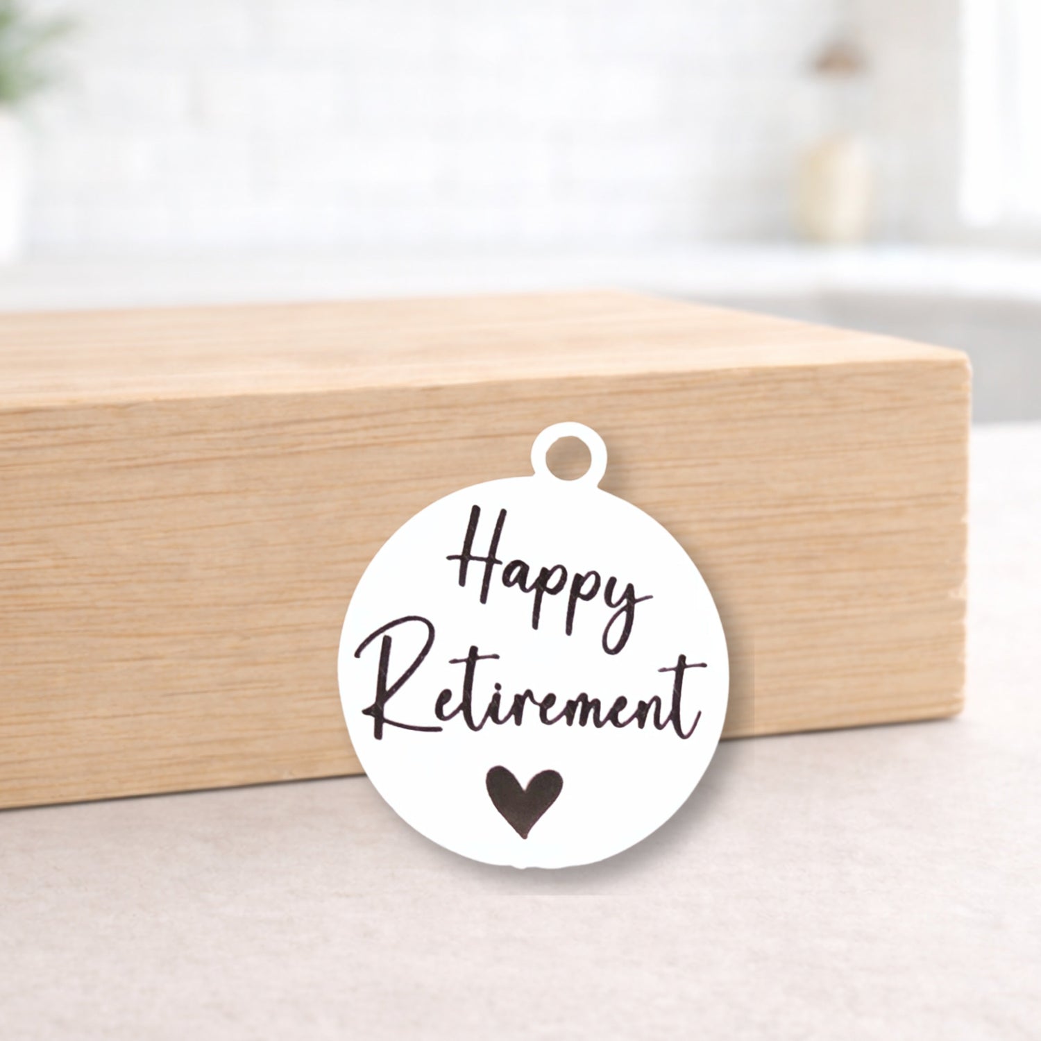 Round white tag with 'Happy Retirement' text and a heart symbol on a wooden block.