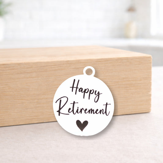 Round white tag with 'Happy Retirement' text and a heart symbol on a wooden block.