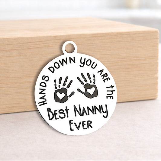 Round white pendant with engraved text and handprints on a wooden block.