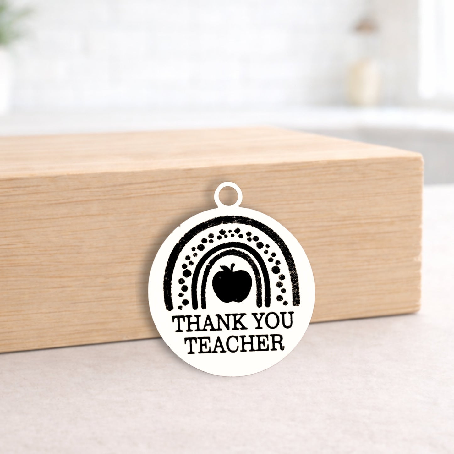 Round white tag with 'Thank You Teacher' text and apple design on a wooden block.
