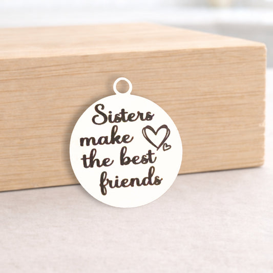 Round white pendant with 'Sisters make the best friends' text on a wooden block.