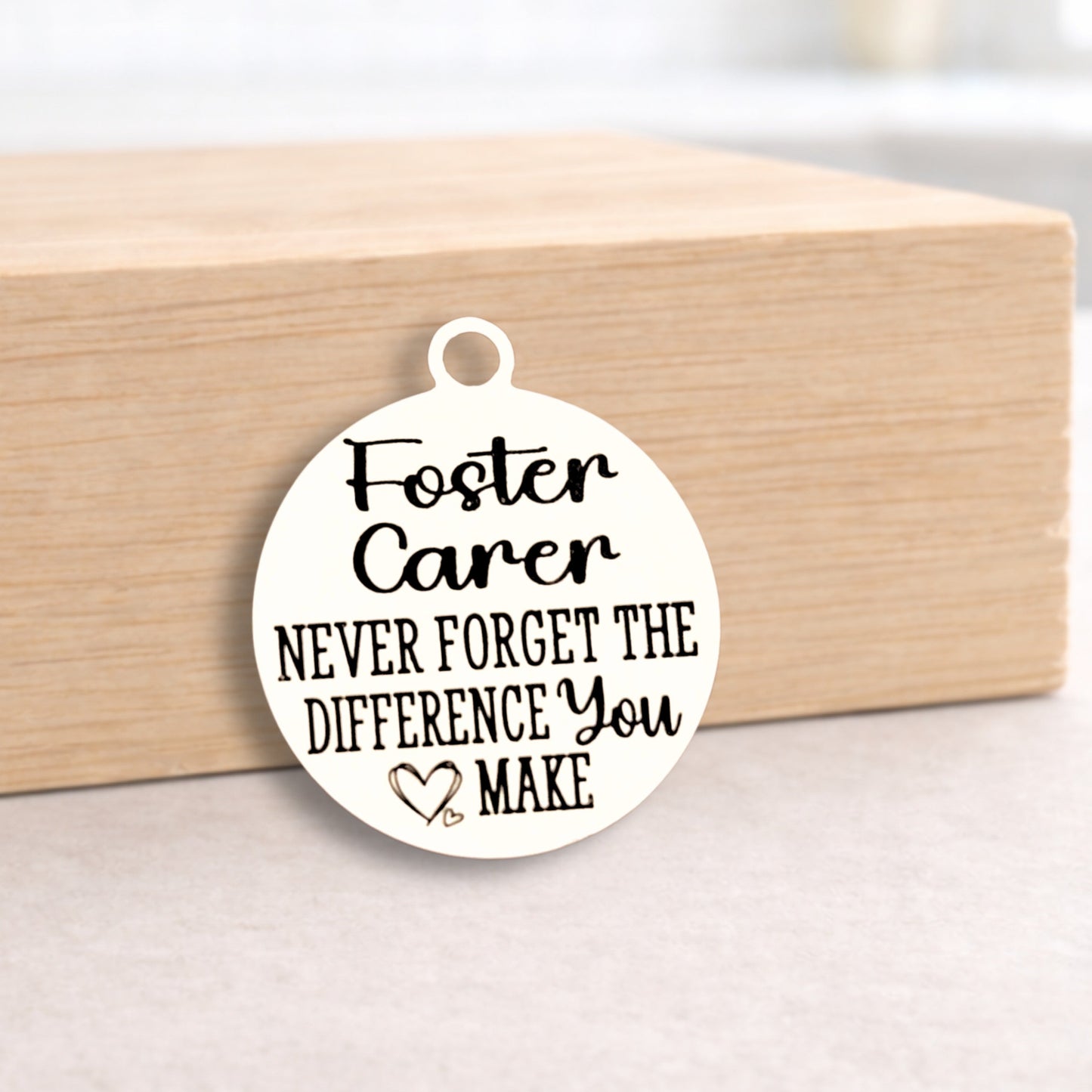 Round pendant with 'Foster Carer Never Forget the Difference You Make' text on a wooden block.
