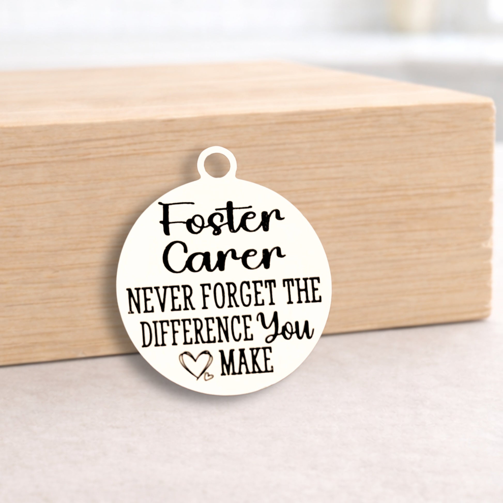 Round pendant with 'Foster Carer Never Forget the Difference You Make' text on a wooden block.